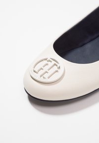 Białe skórzane płaskie buty z okrągłym noskiem, z okrągłym logo w białym kolorze z przodu. Wnętrze jest ciemnogranatowe o gładkiej teksturze.