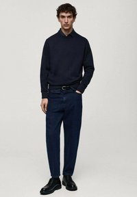 Námornícky sveter s okrúhlym výstrihom, v kombinácii s voľnými tmavomodrými džínsami a čiernymi šnurovacími čižmami, umiestnený na neutrálnom pozadí.