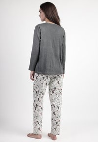 Camiseta gris de manga larga combinada con pantalones de pijama blancos que presentan un estampado juguetón de perros en negro y rojo. Tejido suave, corte relajado y perneras rectas.