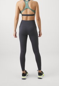 Sportowy strój składający się z miętowej sportowej bielizny z tylnym dekoltem i ciemnoszarych legginsów z wysokim stanem, zestawiony z czarnymi i neonowymi butami biegowymi.