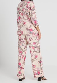 Set di abbigliamento da casa con stampa floreale in morbido tessuto beige, caratterizzato da fiori rosa e accenti scuri. Include una maglietta ampia e pantaloni.