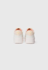 Ein Paar weiße und hellrosa Plateausneaker, von hinten gezeigt, mit Logodetails an der Ferse und der inneren Zunge vor einem weißen Hintergrund.