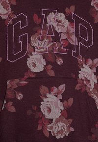 Bordový sweatshirt s velkými vyšitými písmeny "GAP" v růžové barvě. Na textilu se nachází květinové vzory s bílými a červenými růžemi.