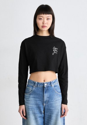 Maglietta nera a maniche lunghe cropped con il testo bianco "Calvin Klein Jeans". Indossata con jeans a gamba larga, a vita alta, in denim blu sbiadito.