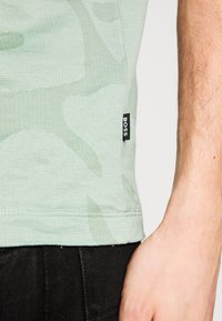 Vaaleanvihreä kuvioitu lyhythihainen paita, jossa on ribbitekstuuri; sivussa on musta "BOSS"-logotagi. Näkyy tummien housujen kanssa.