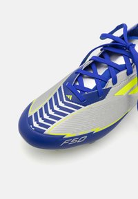 Scarpa da calcio blu e argento con tomaia testurizzata, tacchetti verdi e dettagli gialli. Presenta un motivo a zigzag e il logo 'F50'.