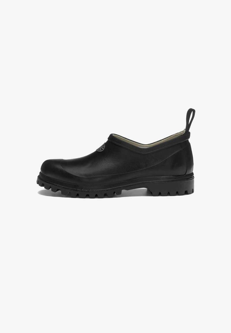 Scarpa nera slip-on con suola robusta, punta tonda, linguetta in tessuto sul tallone e un logo circolare vicino all'apertura della caviglia.