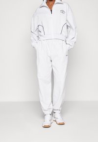 Veste zippée gris clair avec accents noirs et logo, associée à un pantalon de survêtement assorti doté d'une taille élastique et de poignets.}}