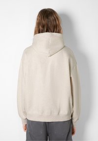 Beige huvtröja med avslappnad passform, som har en stor huva, ribbade ärmslut och nederkant. Den mjuka texturen med en slät yta kompletterar vardagskläder.