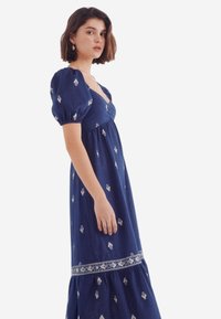 Sinni sinimust maxi kleit lühikeste puhvärvidega, valgete lillemusterdega tikandid, sobiv kehaosa ja kihiline seelik dekoratiivse äärisega.