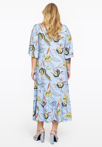 Světle modré květinové maxi šaty s krátkými lehkými rukávy a volánkovým lemem. Obsahují výrazné žluté a černé květinové vzory na měkké látce.