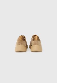 Helle Wildleder-Sneaker mit strukturiertem Rücken, metallischen Goldakzenten und einer beigen Gummisohle. Abgerundete Form, minimalistisches Design.