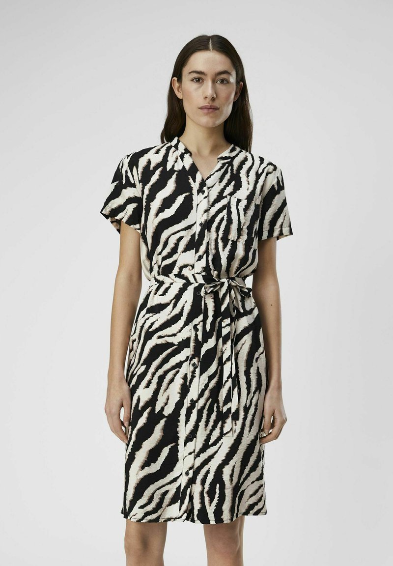 Zwart kortemoffeldress met witte zebraprinten, met een kraag, knoopsluiting aan de voorkant, tailleband en een enkele borstzak.