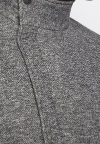 Graue strukturierte Jacke mit hohem Kragen und Knopfverschluss, gefertigt aus einem weichen, gewebten Stoff mit dezentem Melange-Muster.