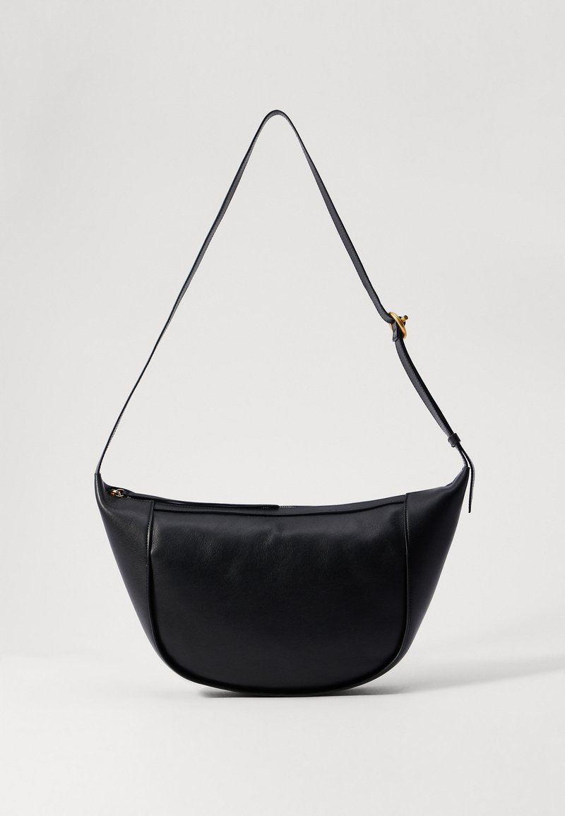 Black leather shoulder bag with a curvy shape, flat base, and a long strap. Features a zipper closure and minimalistic design.
