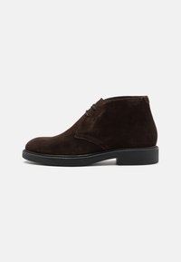 Brown suede ankle boots with a rounded toe, black sole, and minimal lacing. Features a smooth texture and simple design.