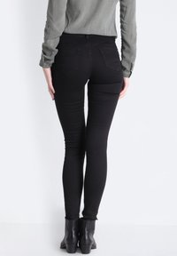 Czarne skinny jeans o gładkiej fakturze, z dwiema tylnymi kieszeniami. Noszone z długim szarym rękawem i czarnymi botkami sięgającymi kostek.