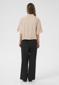 Short-sleeve, light beige top with a collar, paired with high-waisted black wide-leg pants. Smooth texture, minimal design, no visible patterns.