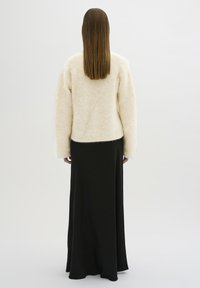 Crème, pluizig sweater met lange mouwen, gecombineerd met een zwarte, vloerlange jurk, die een gladde stof en een eenvoudig ontwerp toont.