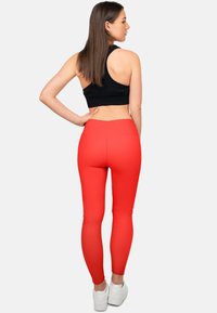 Rode leggings met een hoge taille en elastische stof, gecombineerd met een zwart mouwloos crop top. Het model draagt witte sneakers.