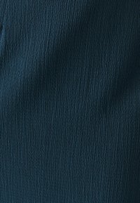 Tissu texturé en bleu sarcelle foncé avec des nervures verticales. Surface lisse avec un léger éclat, adapté pour des vêtements ou de la tapisserie.