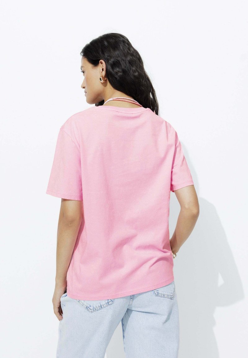 T-shirt en coton rose clair à manches courtes avec une coupe décontractée, présentant un col rond simple et un minimum de détails.