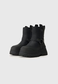 Czarne, masywne botki na platformie z kostką, z uchwytami do zakupu, detalami w postaci pasków i chropowatą, teksturowaną podeszwą na białym tle.