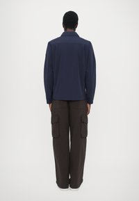 Navy long-sleeve shirt with a relaxed fit, paired with dark brown cargo pants featuring multiple pockets and a slightly textured fabric.
