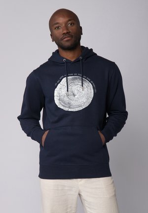 Marineblauwe hoodie met een voorzak in kangoeroestijl, voorzien van een cirkelvormige boomringgrafiek in zilver en tekst die het ontwerp omsluit. Gemaakt van een katoenmix.