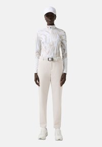 Dlouhý rukáv s abstraktním krémovým vzorem, vysoký límec a poloviční zapínání na zip. Lehký krémový kalhoty s páskem. Bílé tenisky a čepice.