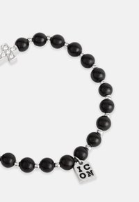 Brățară din mărgele negre cu accente din argint, o cruce împodobită cu strasuri și o etichetă metalică gravată cu "ICON."