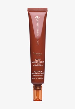 Brązowa tubka Danessa Myricks Beauty Yummy Skin 10/10 Barrier Boost serum nawilżające do wzmocnienia bariery ochronnej, 50 ml z pomarańczowym aplikatorem w formie kulki.