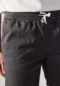 Pantalones cortos de algodón grises con cintura elástica, que cuentan con un cordón blanco, un bolsillo lateral y una textura suave.