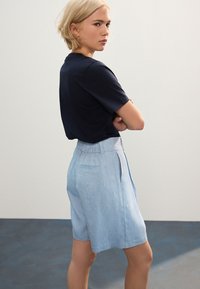 Camicia a maniche corte blu navy abbinata a pantaloncini a vita alta di colore azzurro chiaro con trama, caratterizzati da una tasca posteriore e da un design frontale liscio.