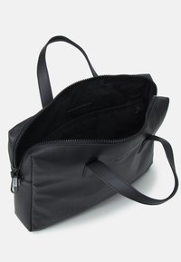Black leather bag with a textured surface, zip closure, two handles, and a spacious interior featuring pockets for organization.