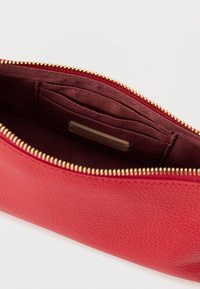 Crvena kožna torbica s teksturiranom površinom, zlatnim patentnim zatvaračem i bordo postavom s utorima za kartice. Kompaktan i funkcionalan dizajn.