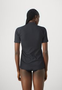 Black ribbed short-sleeve top with a high neckline, made from stretchy material. Features fitted design and subtle brand detailing at hem.