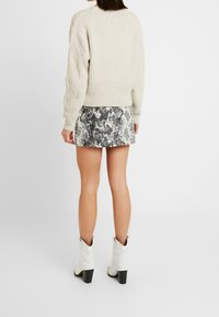 Chunky gebreide crème trui met textuursleeves, gecombineerd met een aansluitende minirok in zwart-wit slangenprint en witte western enkellaarsjes.