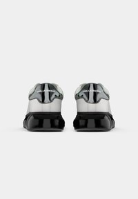 Adidași negri și gri cu un superior din piele netedă, accente reflective și o talpă lucioasă neagră, cu o secțiune contrastantă bej.