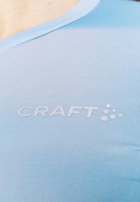 Ljusblå träningsskjorta med en slät, elastisk textur. Har en rund halsringning och debossat "CRAFT"-logotyp på framsidan.