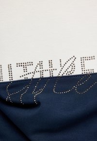 Navy and cream top featuring a smooth fabric blend, with decorative metallic studs arranged in text patterns. Distinct two-tone color scheme.