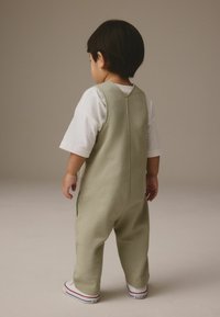 Combinaison en coton vert clair avec un dos en V, des poignets élastiques et une coupe loose. Assortie à des baskets blanches avec des accents rouges.