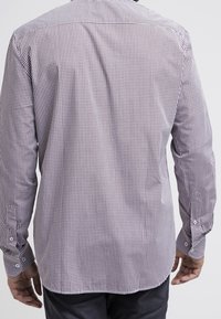 Mann, der ein langärmliges, knopfbares, klein kariertes Hemd in Rot und Weiß trägt, von hinten gesehen.