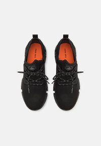 Zapatillas deportivas negras con una parte superior de malla texturizada, cordones reflectantes y una plantilla acolchada naranja. Destacan por su diseño elegante y moderno.