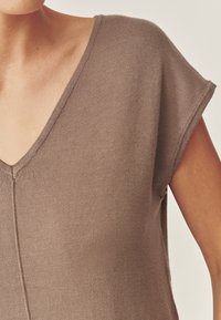 Braunes, kurzärmeliges Strickoberteil mit V-Ausschnitt, glatter Textur und dezenten Nahtdetails entlang der Mitte und der Ärmel.