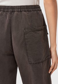 Pantaloni marroni scuri con vestibilità comoda, dotati di una cintura elastica, tasche laterali e un tessuto morbido e testurizzato con dettagli di cucitura discreti.