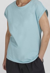 Light blue short-sleeve t-shirt made from soft cotton fabric. Crew neck design with rolled sleeves, relaxed fit, and subtle drape.