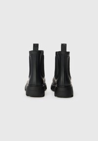 Bottes Chelsea en caoutchouc noir avec panneaux latéraux élastiques et tirettes. Semelle texturée et marquage subtil au niveau du talon. Fini lisse.