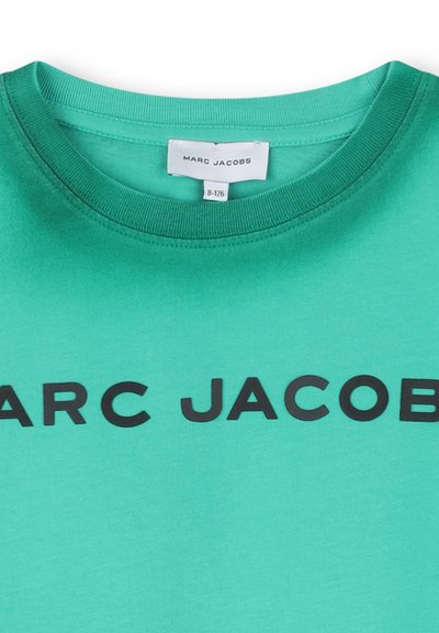 Groen shirt met ronde hals en zwarte tekst "MARC JACOBS" over de borst, met een wit label aan de binnenkant van de kraag waarop de merknaam staat.