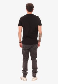 T-shirt nera in cotone con scollatura rotonda, abbinata a jeans in denim grigi. L'outfit è completato da sneakers bianche e braccialetti.